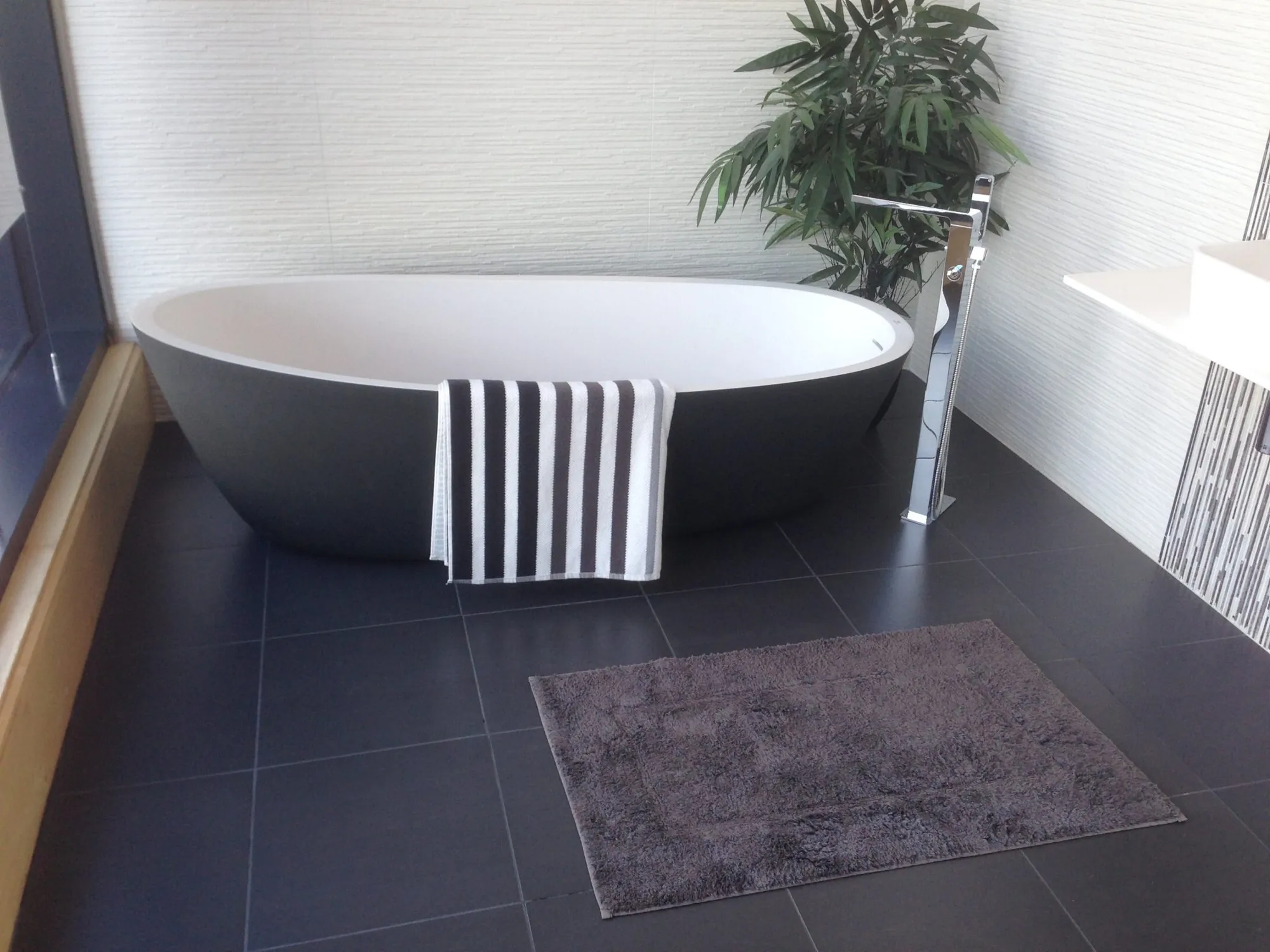 Freestanding tub on a dark porcelain tile floor with a gray bath mat